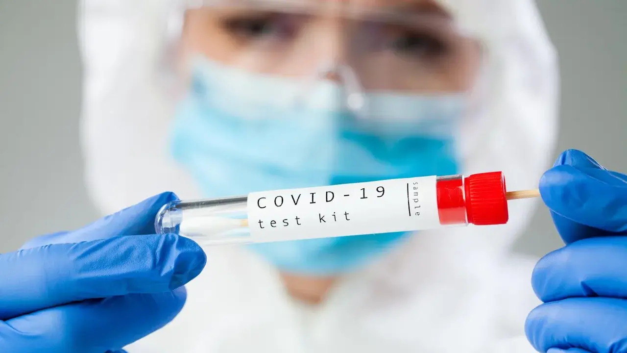 Osoba w kombinezonie i rękawiczkach trzyma probówkę z wymazem. Zastanawiasz się, ile kosztuje test na covid?