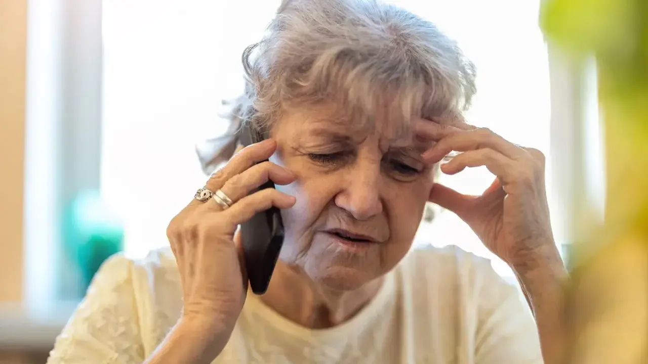 Zmartwiona starsza pani rozmawia przez telefon, dowiadując się o nowe zasady wyjazdu do sanatorium na NFZ.