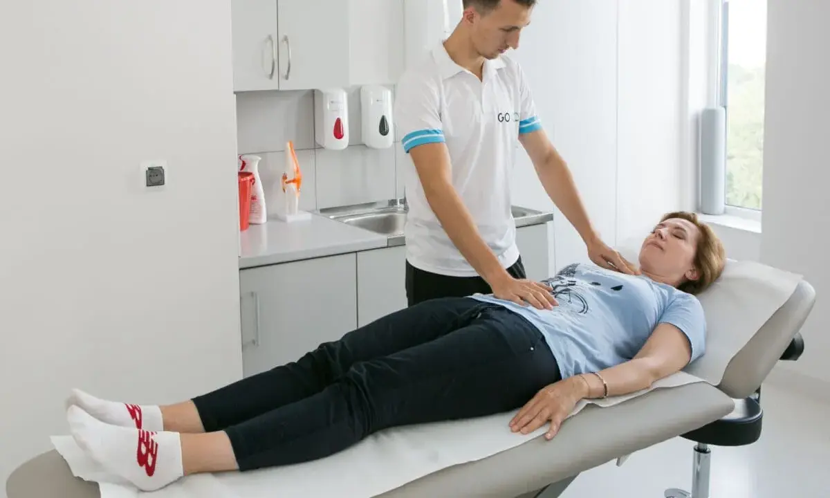 Fizjoterapeuta pomaga pacjentce w ćwiczeniach oddechowych, kładąc dłonie na jej klatce piersiowej i brzuchu.