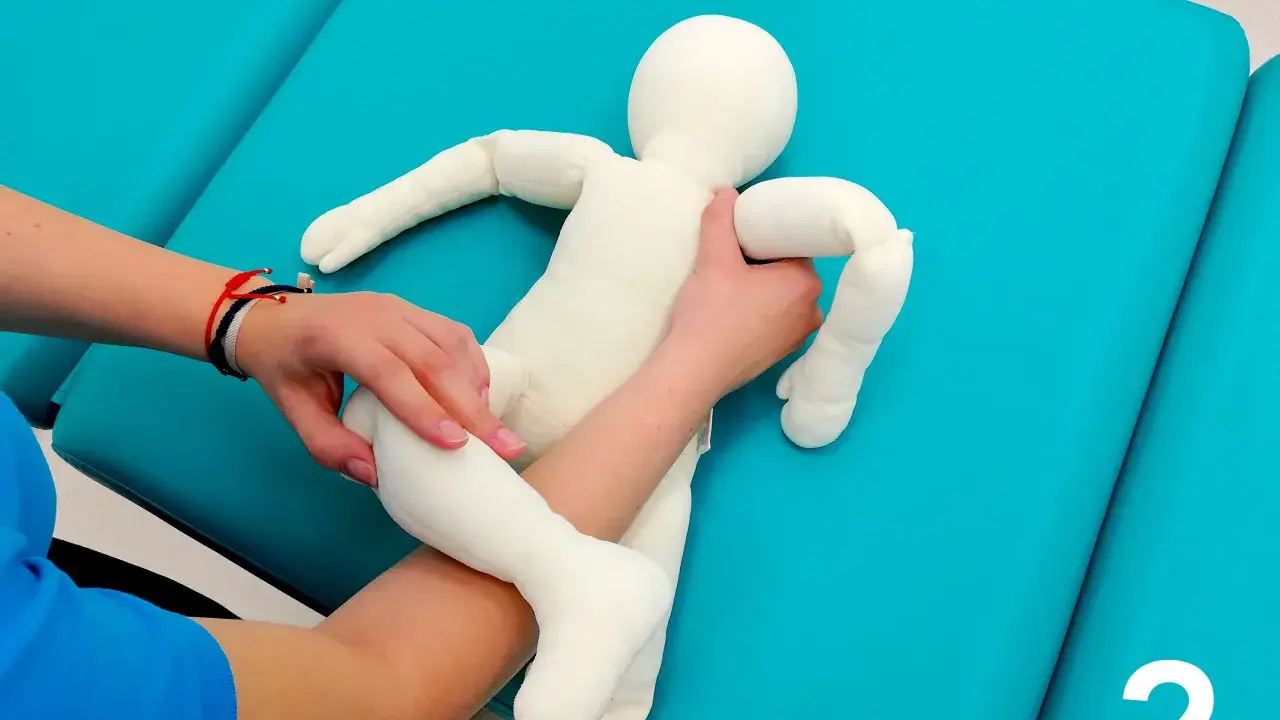 Fizjoterapeuta pokazuje mamie, jak podnosić niemowlę, trzymając pluszową lalkę.