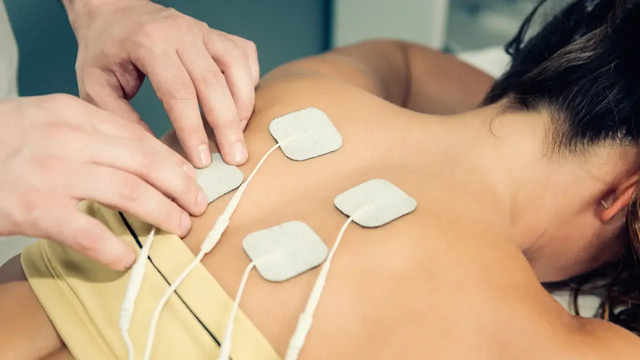 Rehabilitacja TENS: na czym polega? Fizjoterapeuta umieszcza elektrody na plecach pacjentki, co jest częścią terapii prądami TENS.