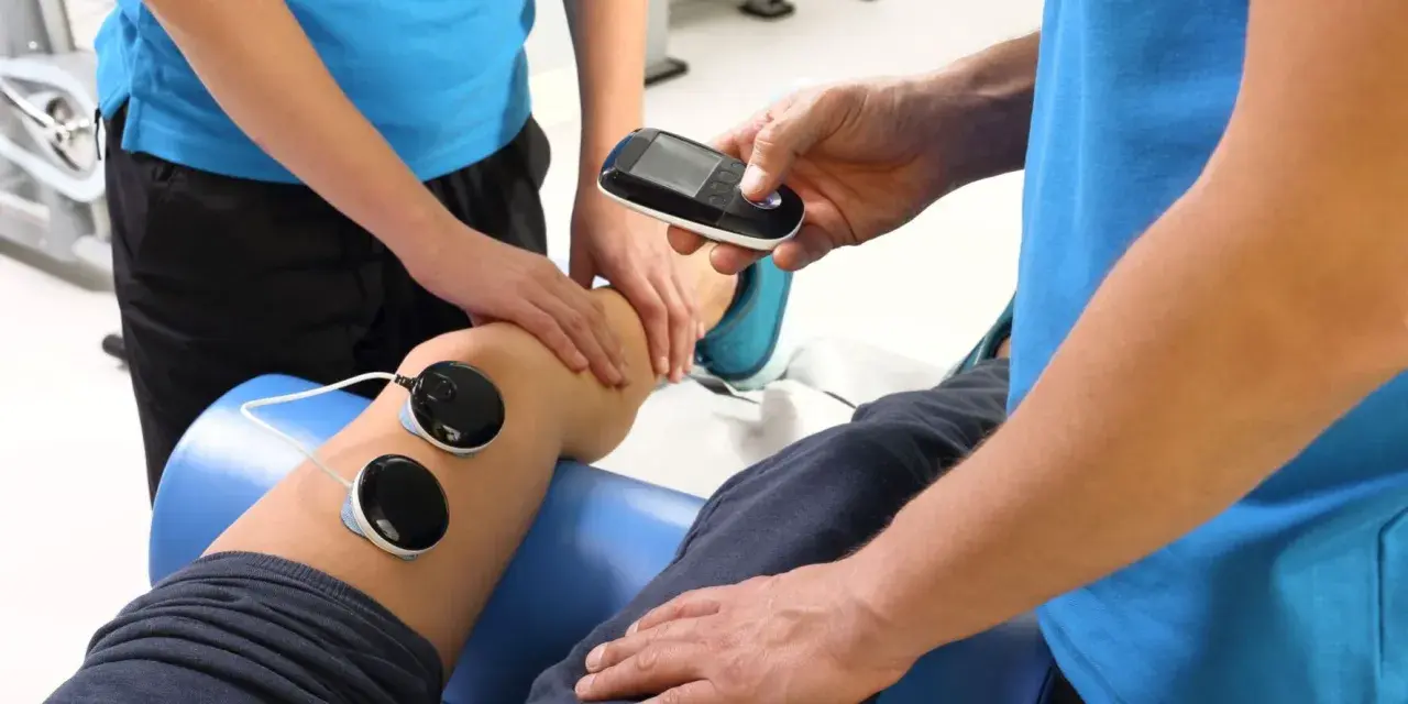 Fizjoterapeuta z urządzeniem do elektroterapii przy nodze pacjenta. Ile razy w roku można korzystać z rehabilitacji szpitalnej?