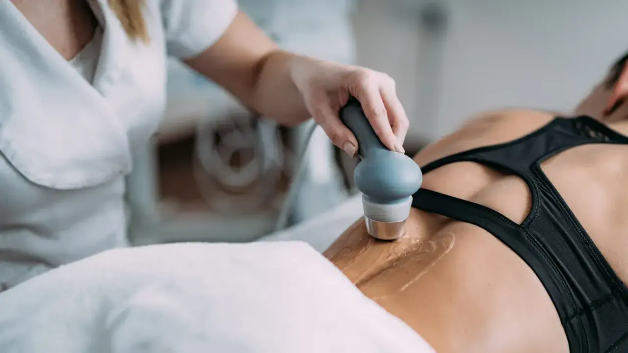 Fizjoterapeuta stosuje głowicę do terapii ultradźwiękami na plecy pacjentki, wspomagając regenerację.