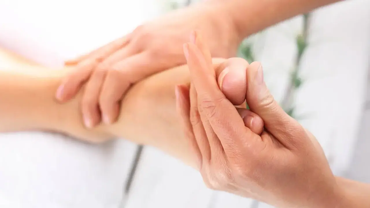 Dłoń terapeuty masuje stopę pacjenta, skupiając się na palcach.