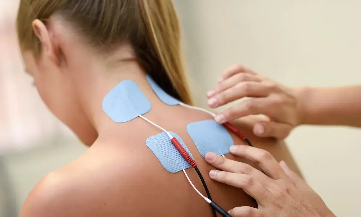 Elektrody na plecach kobiety, podłączone do urządzenia. To przykład, co to jest fizjoterapia – rehabilitacja i leczenie bólu.