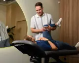 Fizjoterapeuta pomaga pacjentowi w ćwiczeniach nogi, co jest kluczowe w pytaniu: ile trwa rehabilitacja po artroskopii stawu skokowego.