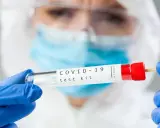 Osoba w kombinezonie i rękawiczkach trzyma probówkę z wymazem. Zastanawiasz się, ile kosztuje test na covid?