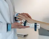 Lekarz zakłada ortezę na rękę pacjenta, co jest kluczowe w procesie, ile trwa rehabilitacja po złamaniu ręki.