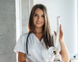 Uśmiechnięta fizjoterapeutka z modelem kręgosłupa. Zastanawia się, do kiedy studia magisterskie fizjoterapia.