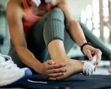 Kobieta masuje bolącą kostkę w siłowni, obok leży but sportowy.