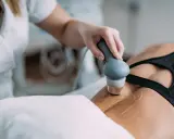 Rehabilitacja ultradźwięki na czym polega? Fizjoterapeuta wykonuje zabieg ultradźwiękami na plecach pacjentki, co pomaga w leczeniu bólu i regeneracji tkanek.