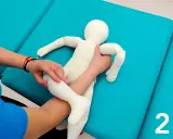 Fizjoterapeuta pokazuje mamie, jak podnosić niemowlę, trzymając pluszową lalkę.