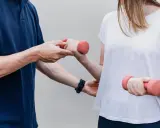 Fizjoterapeuta pomaga pacjentce ćwiczyć z hantlami. To przykład rehabilitacji, która przywraca sprawność.