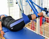 Kobieta na łóżku rehabilitacyjnym ćwiczy nogi w systemie podwieszeń. To przykład, jak wygląda rehabilitacja dzienna co to jest.