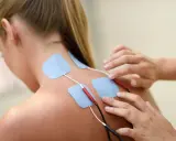 Elektrody na plecach kobiety, podłączone do urządzenia. To przykład, co to jest fizjoterapia – rehabilitacja i leczenie bólu.
