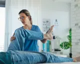 Fizjoterapeutka wykonuje ćwiczenia z pacjentem, pomagając mu w rehabilitacji. Długie **NFZ terminy leczenia** mogą być frustrujące, ale profesjonalna opieka jest kluczowa.