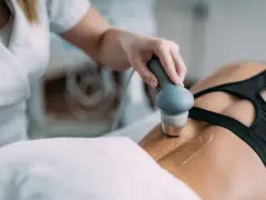 Fizjoterapeuta wykonuje zabieg ultradźwiękami na plecach pacjentki, stosując żel do lepszego przewodzenia fal.