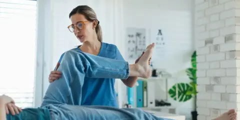 Fizjoterapeutka bada nogę pacjenta. Czy do fizjoterapeuty potrzebne jest skierowanie? Zależy od placówki.