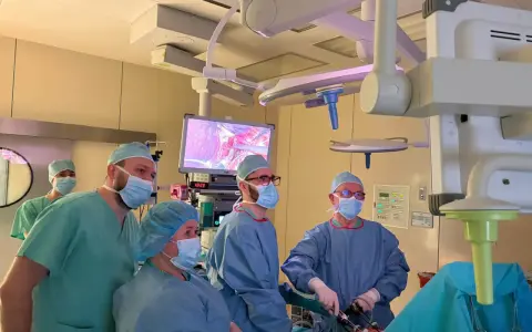 Zespół chirurgów w maseczkach i czepkach podczas operacji, patrzący na monitor z obrazem z wnętrza ciała.