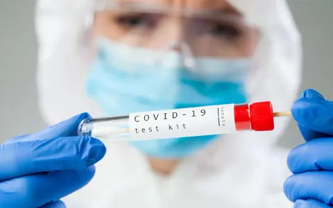 Osoba w kombinezonie i rękawiczkach trzyma probówkę z wymazem. Zastanawiasz się, ile kosztuje test na covid?