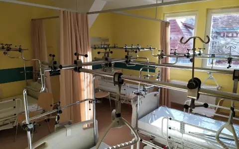Szpitalna sala z łóżkami i aparaturą ortopedyczną.