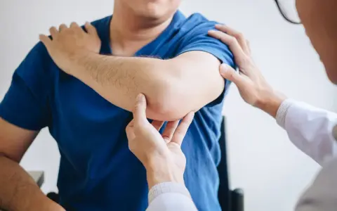 Fizjoterapeuta bada łokieć pacjenta. Dłonie specjalisty delikatnie dotykają bolącego miejsca, oceniając zakres ruchu i ból.