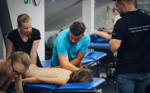Uczestnicy szkolenia doskonalą technikę masażu tkanek głębokich, pracując nad plecami pacjenta.