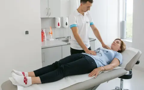 Fizjoterapeuta pomaga pacjentce w ćwiczeniach oddechowych, kładąc dłonie na jej klatce piersiowej i brzuchu.