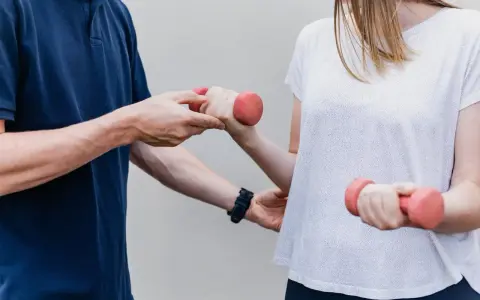 Fizjoterapeuta pomaga pacjentce ćwiczyć z hantlami. To przykład rehabilitacji, która przywraca sprawność.