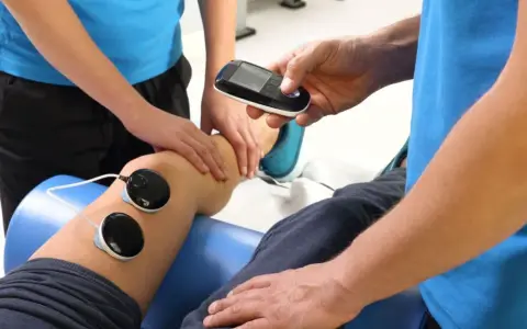 Fizjoterapeuta z urządzeniem do elektroterapii przy nodze pacjenta. Ile razy w roku można korzystać z rehabilitacji szpitalnej?