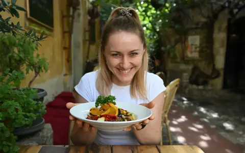 Uśmiechnięta kobieta prezentuje talerz pełen kolorowych warzyw, idealnych na dietę śródziemnomorską.