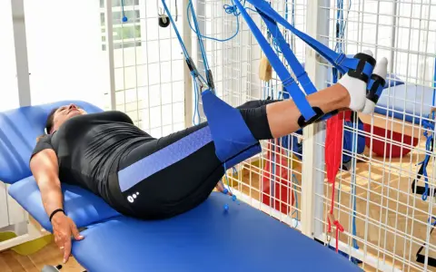 Kobieta na łóżku rehabilitacyjnym ćwiczy nogi w systemie podwieszeń. To przykład, jak wygląda rehabilitacja dzienna co to jest.