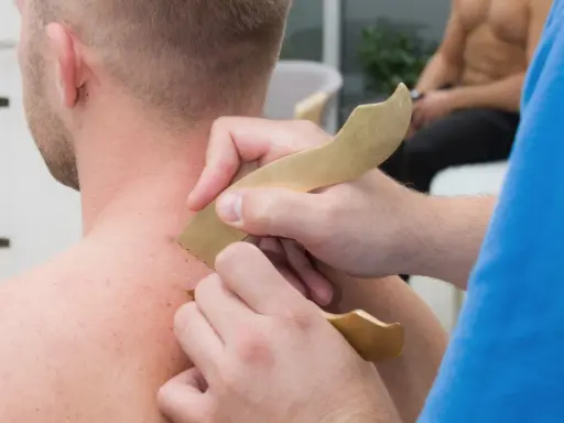 Masaż karku z użyciem narzędzi do pinoterapii. Terapeuta wykonuje zabieg na skórze pacjenta.