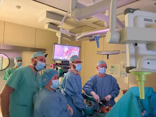 Zespół chirurgów w maseczkach i czepkach podczas operacji, patrzący na monitor z obrazem z wnętrza ciała.