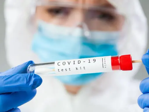 Osoba w kombinezonie i rękawiczkach trzyma probówkę z wymazem. Zastanawiasz się, ile kosztuje test na covid?