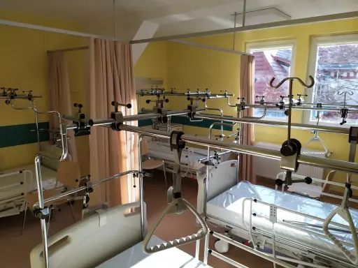 Szpitalna sala z łóżkami i aparaturą ortopedyczną.