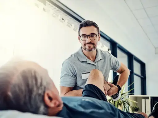 Fizjoterapeuta pomaga pacjentowi w ćwiczeniach rehabilitacyjnych, by odzyskać sprawność.