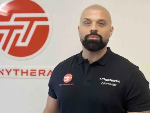 Tomasz Chachurski w czarnej koszulce z logo Toonytherapy, na tle białej ściany z logo.