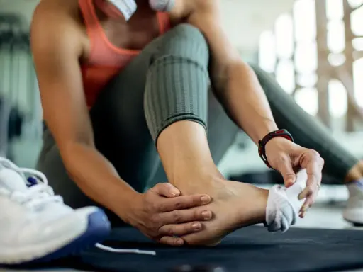 Kobieta masuje bolącą kostkę w siłowni, obok leży but sportowy.