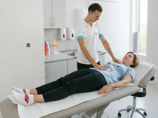 Fizjoterapeuta pomaga pacjentce w ćwiczeniach oddechowych, kładąc dłonie na jej klatce piersiowej i brzuchu.