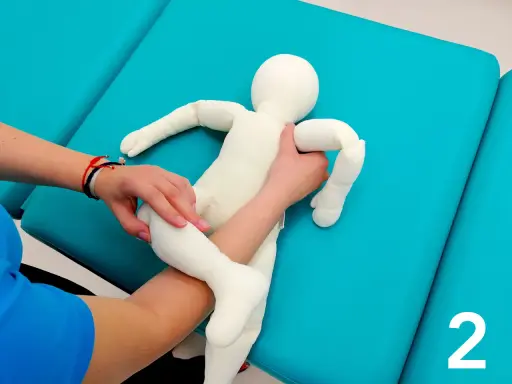 Fizjoterapeuta pokazuje mamie, jak podnosić niemowlę, trzymając pluszową lalkę.
