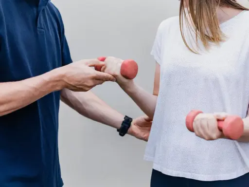 Fizjoterapeuta pomaga pacjentce ćwiczyć z hantlami. To przykład rehabilitacji, która przywraca sprawność.