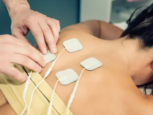 Rehabilitacja TENS: na czym polega? Fizjoterapeuta umieszcza elektrody na plecach pacjentki, co jest częścią terapii prądami TENS.