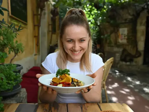 Uśmiechnięta kobieta prezentuje talerz pełen kolorowych warzyw, idealnych na dietę śródziemnomorską.