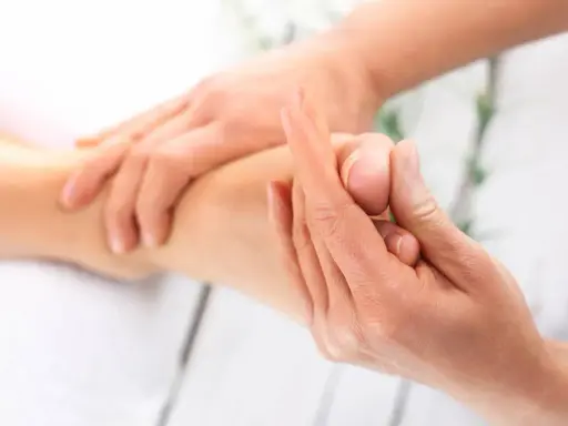 Dłoń terapeuty masuje stopę pacjenta, skupiając się na palcach.