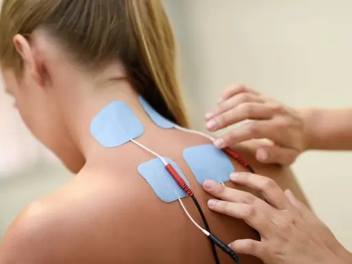 Elektrody na plecach kobiety, podłączone do urządzenia. To przykład, co to jest fizjoterapia – rehabilitacja i leczenie bólu.
