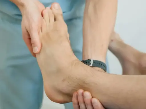 Fizjoterapeuta bada stopę pacjenta, oceniając, ile czasu trwa rehabilitacja po złamaniu.