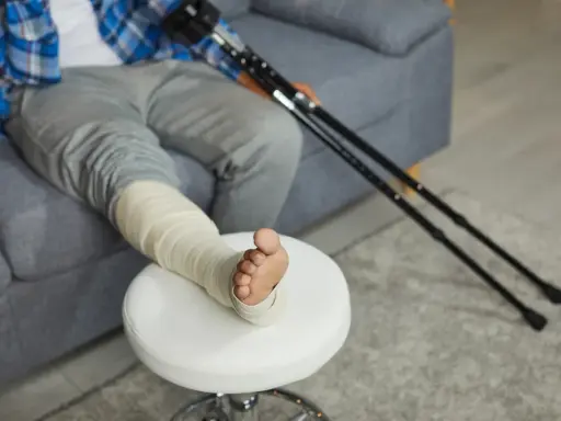 Osoba z zabandażowaną nogą i kulami obok, przygotowuje się do zgłoszenia skręcenia stawu skokowego do PZU.
