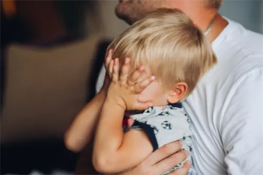 Małe dziecko zakrywa twarz dłońmi, tulone przez ojca. Czy to objawy PTSD?