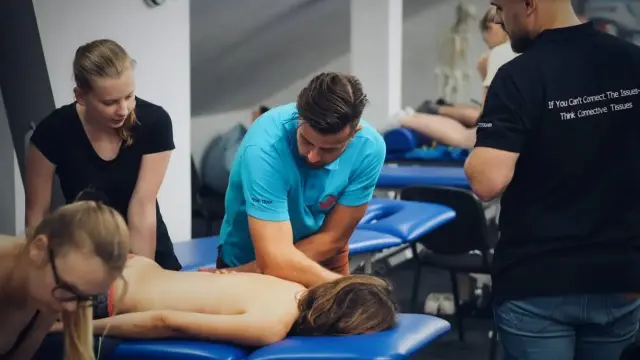 Uczestnicy szkolenia doskonalą technikę masażu tkanek głębokich, pracując nad plecami pacjenta.
